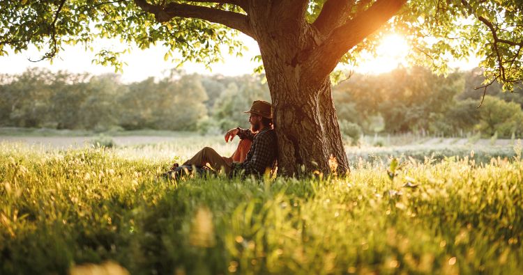 A young man sits calmly against a tree