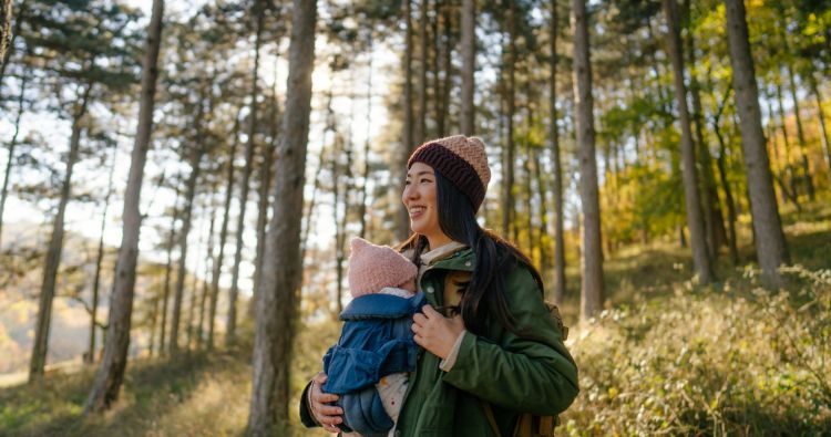 A woman wears her baby while hiking through the woods.