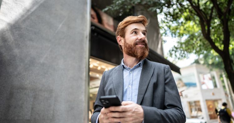 A man in a business suit walks through a city texting on his phone